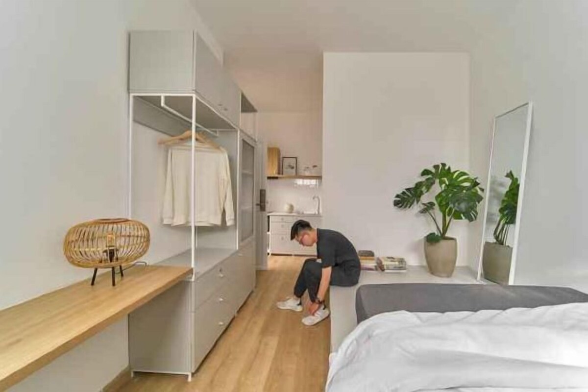 Une chambre à coucher de taille réduite, comprenant un lit, une table de chevet, une armoire et une plante en pot.