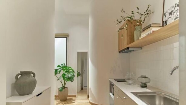 A modern kitchen with white cabinets, a stainless steel sink, and a wooden shelf with decorative items. - Express by M Village Nguyen Du, a brand of Modern Village Lifestyle (Ho Chi Minh City)