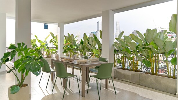 A modern dining area with a table set for four, surrounded by potted plants and overlooking a cityscape. - Express by M Village Nguyen Du, a brand of Modern Village Lifestyle (Ho Chi Minh City)