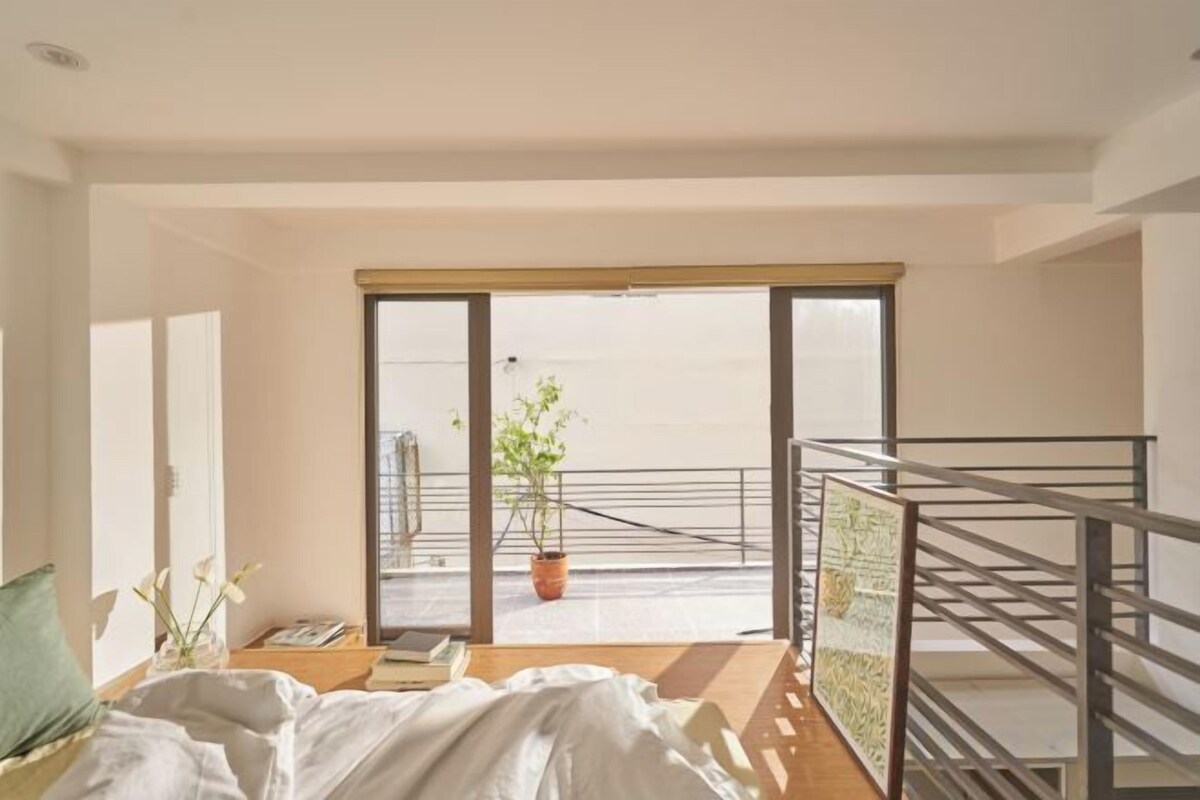 A bedroom with a bed, a potted plant, and a view of the outside balcony.