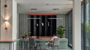 A modern reception desk with two chairs, a glass partition, and a plant. - Express by M Village Nguyen Du, a brand of Modern Village Lifestyle (Ho Chi Minh City)