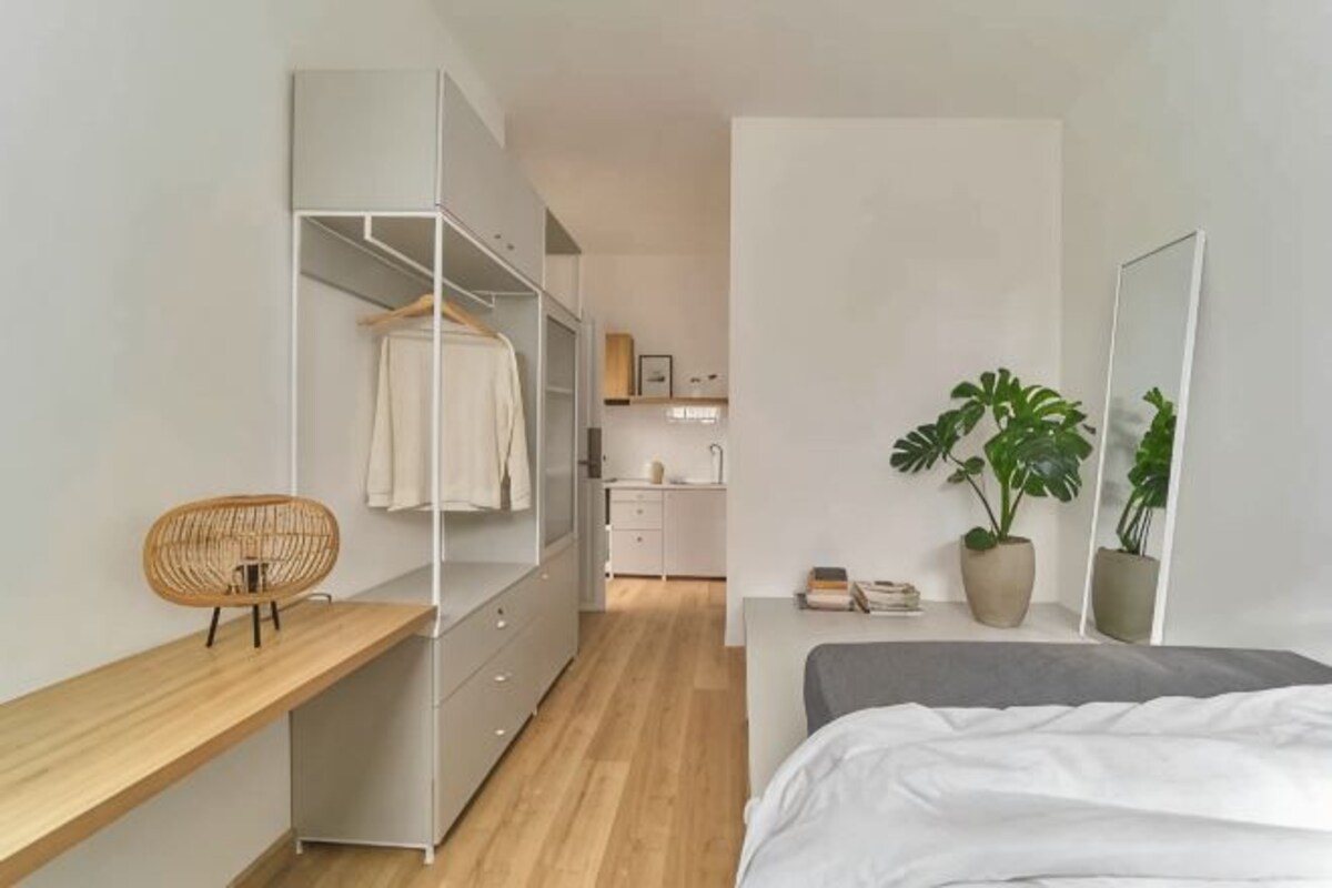Une chambre à coucher comprenant un lit, une table de chevet, une armoire, un fauteuil suspendu, une plante en pot et un miroir.