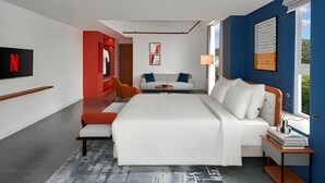 Ein modernes Hotelzimmer mit einem großen Bett, einer Sitzecke, einem Fernseher und Kunstwerken an den Wänden.