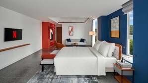 Ein modernes Hotelzimmer mit einem großen Bett, einem Fernseher, einer Sitzecke und Blick ins Freie.