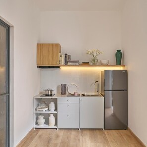 Een compacte keuken met witte kastjes, een roestvrijstalen koelkast en een houten plank boven het aanrecht.