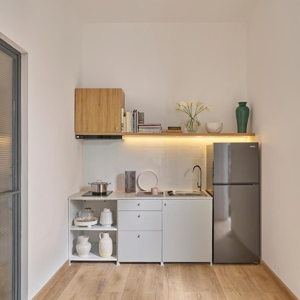 Une cuisine de taille réduite avec des meubles blancs, un réfrigérateur en acier inoxydable et une étagère en bois au-dessus du plan de travail.
