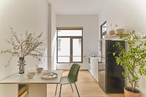 A modern kitchen with a black refrigerator, a dining table with chairs, and a window with blinds. - Express by M Village Nguyen Du, a brand of Modern Village Lifestyle (Ho Chi Minh City)