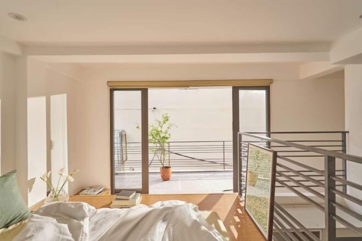 Une pièce avec un lit, une fenêtre, une plante et une vue sur l’extérieur.