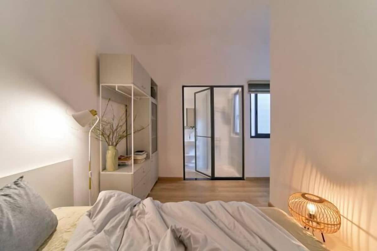 Une chambre à coucher comprenant un lit, une table de chevet, une lampe, une armoire et une porte coulissante donnant sur une autre pièce.