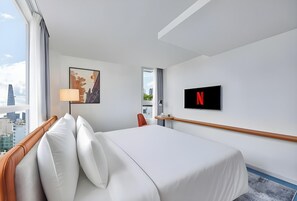 Een hotelkamer met een bed, een televisie, een schilderij en uitzicht over de stad.