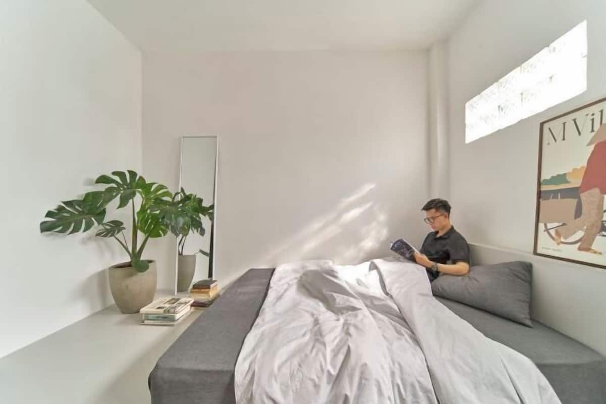 Une chambre à coucher moderne avec un lit, une plante en pot, un miroir et une œuvre d’art accrochée au mur.