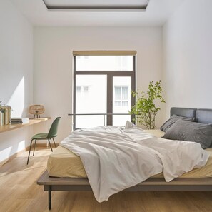 A bedroom with a bed, a chair, a plant, and a window. - Express by M Village Nguyen Du, a brand of Modern Village Lifestyle (Ho Chi Minh City)