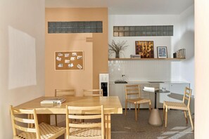 Een eetruimte met een houten tafel en stoelen, een prikbord en een keuken met witte kasten en een betegelde achterwand.