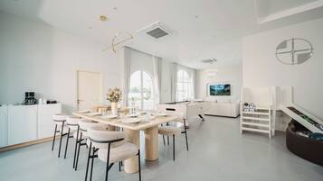 A modern, well-lit dining area with a pool table, comfortable seating, and a kitchen area with white cabinetry.