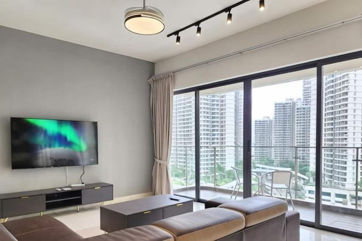 A modern living room with a TV, sofa, and large windows overlooking a cityscape.