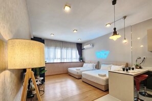 A modern hotel room with a sofa, a small dining table, a lamp, and a TV. - Country Garden Danga Bay NEO Suites (Johor Bahru)