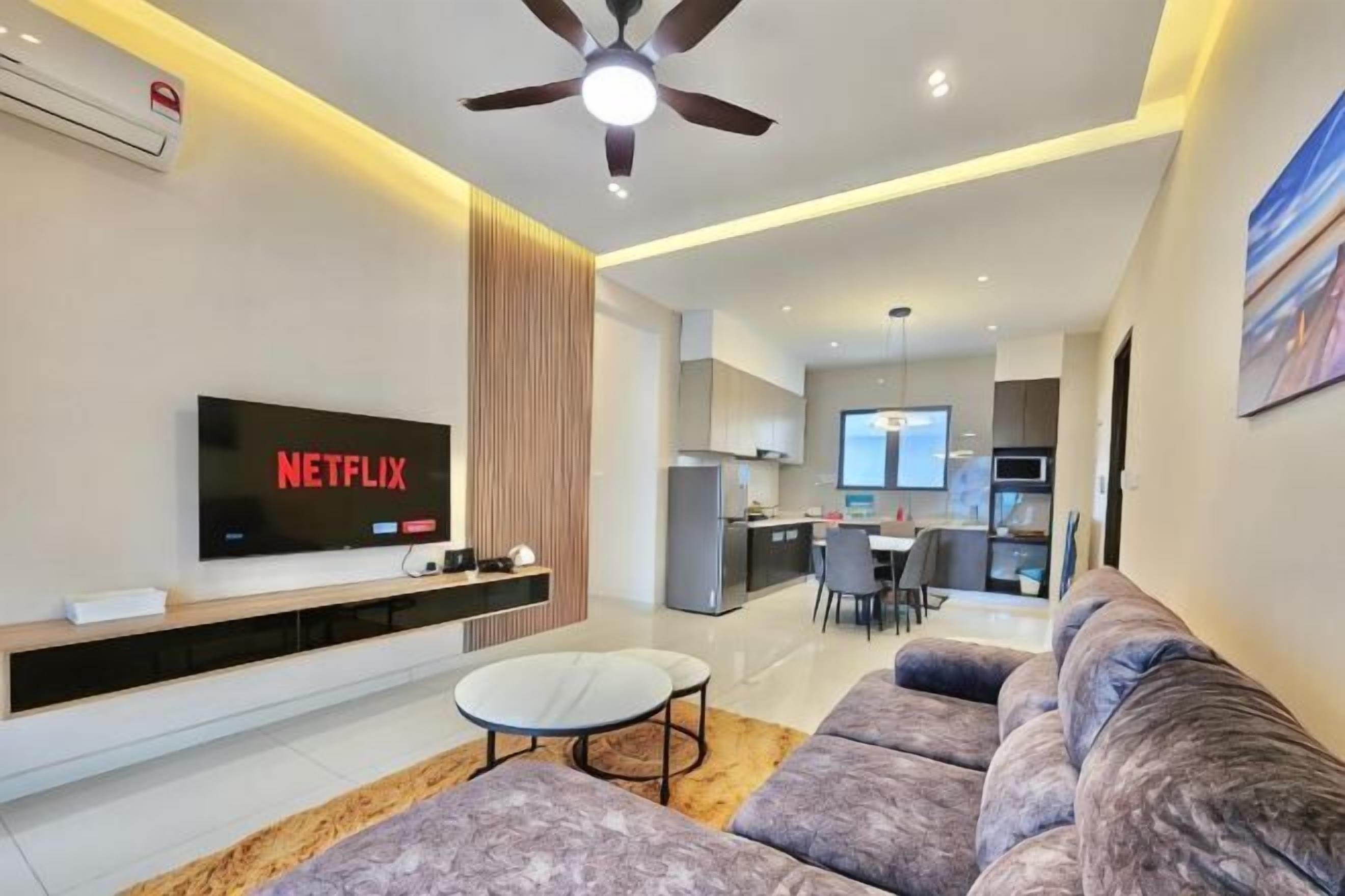 A modern living room with a flat-screen TV, a ceiling fan, a sofa, and a dining area in the background.
