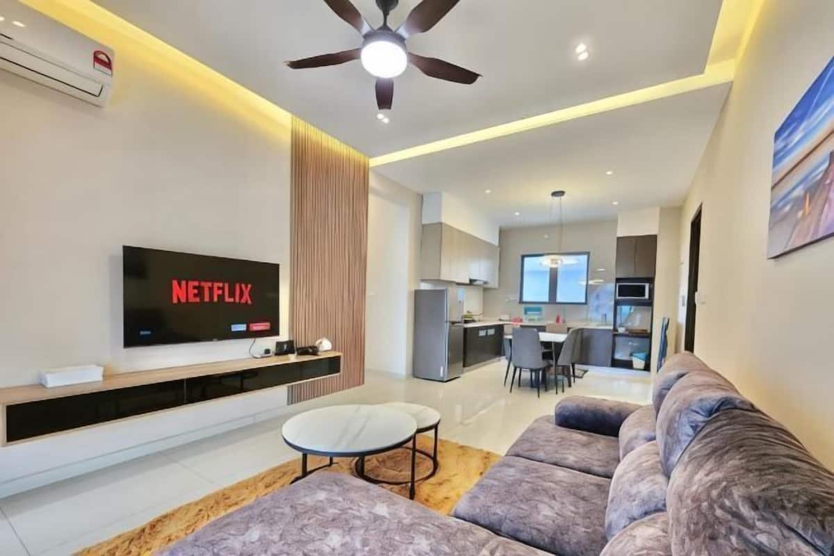 A modern living room with a flat-screen TV, a ceiling fan, a sofa, and a dining area in the background.