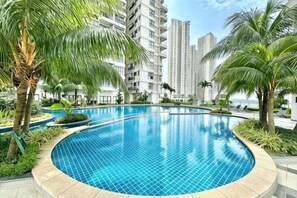 A swimming pool with a curved edge, surrounded by palm trees and greenery, with tall buildings in the background. - Country Garden Danga Bay NEO Suites (Johor Bahru)