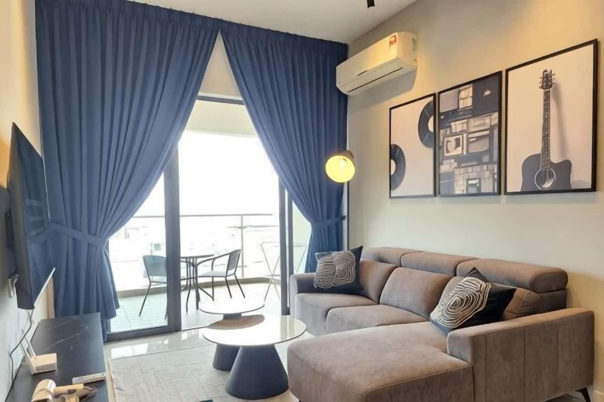 A living room with a sofa, a coffee table, a TV, and a balcony with blue curtains.