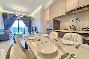 Un comedor moderno con una mesa larga dispuesta para cuatro personas, un sofá y una cocina con estufa y microondas.