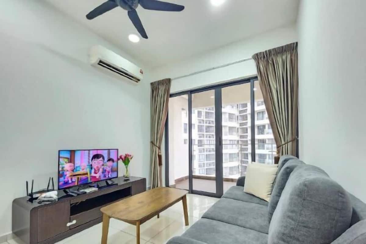 A living room with a flat-screen TV, a ceiling fan, and a large window with curtains.