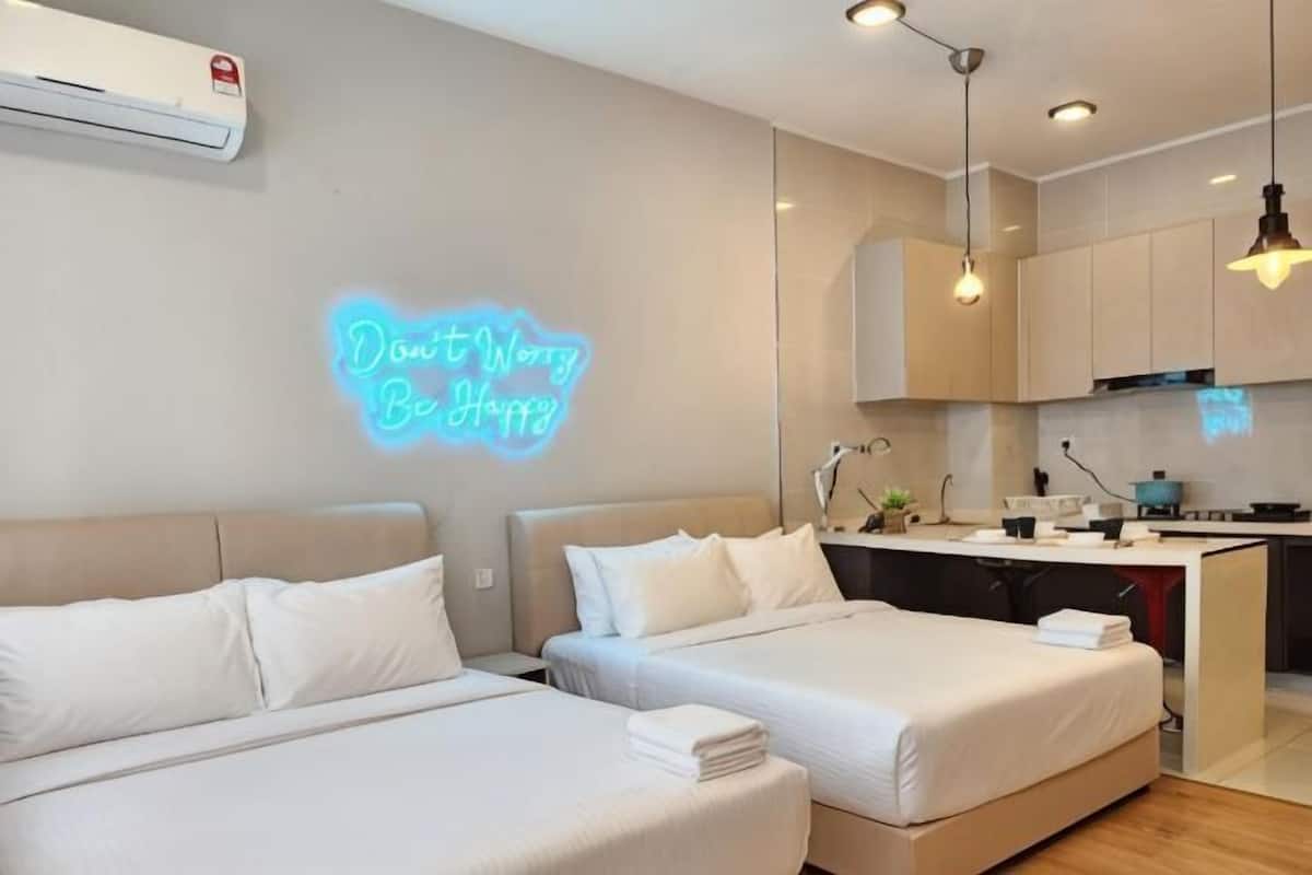 A modern hotel room with two beds, a kitchen area, and a neon sign on the wall.