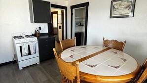 A dining area with a round table, wooden chairs, a ceiling fan, and a kitchen in the background.