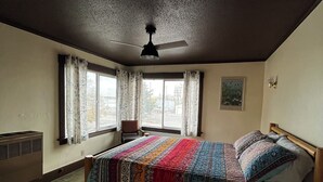 A bedroom with a bed, a ceiling fan, a window with curtains, and a radiator.