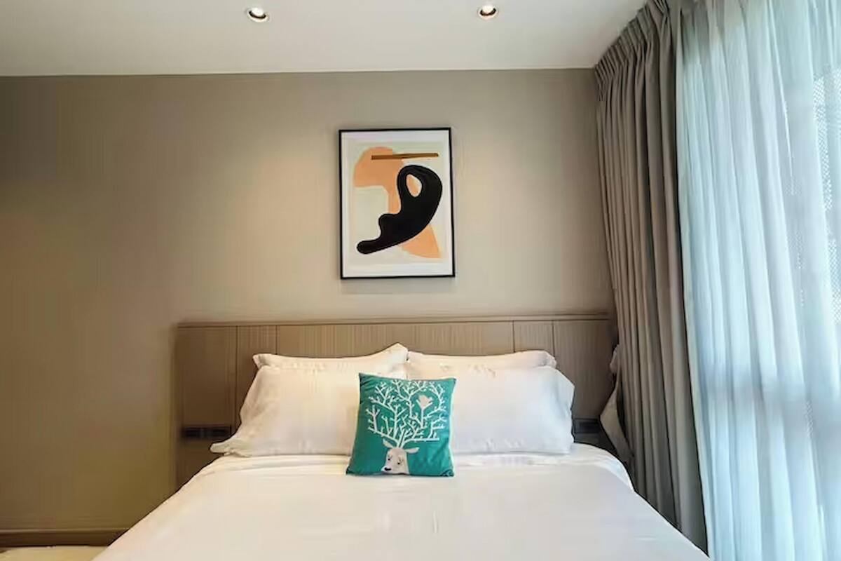 A hotel room with a bed, a headboard, a wall-mounted artwork, and a window with curtains.