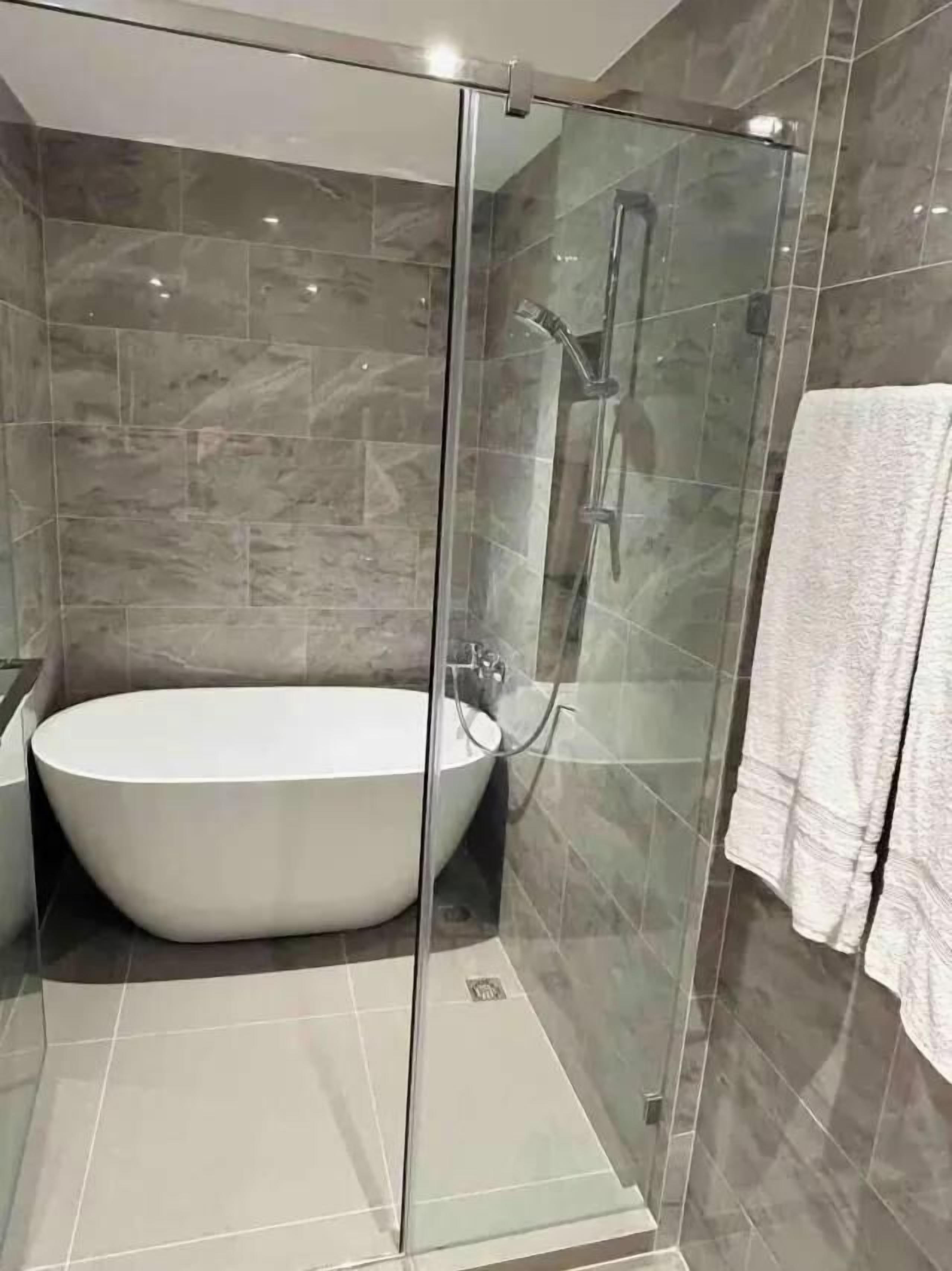 A modern bathroom with a glass-enclosed shower, a freestanding bathtub, and a towel rack.
