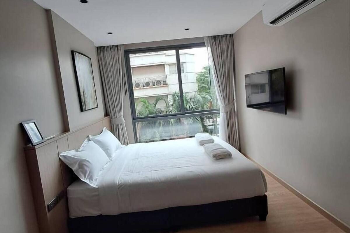 A hotel room with a bed, a TV mounted on the wall, and a window with curtains.