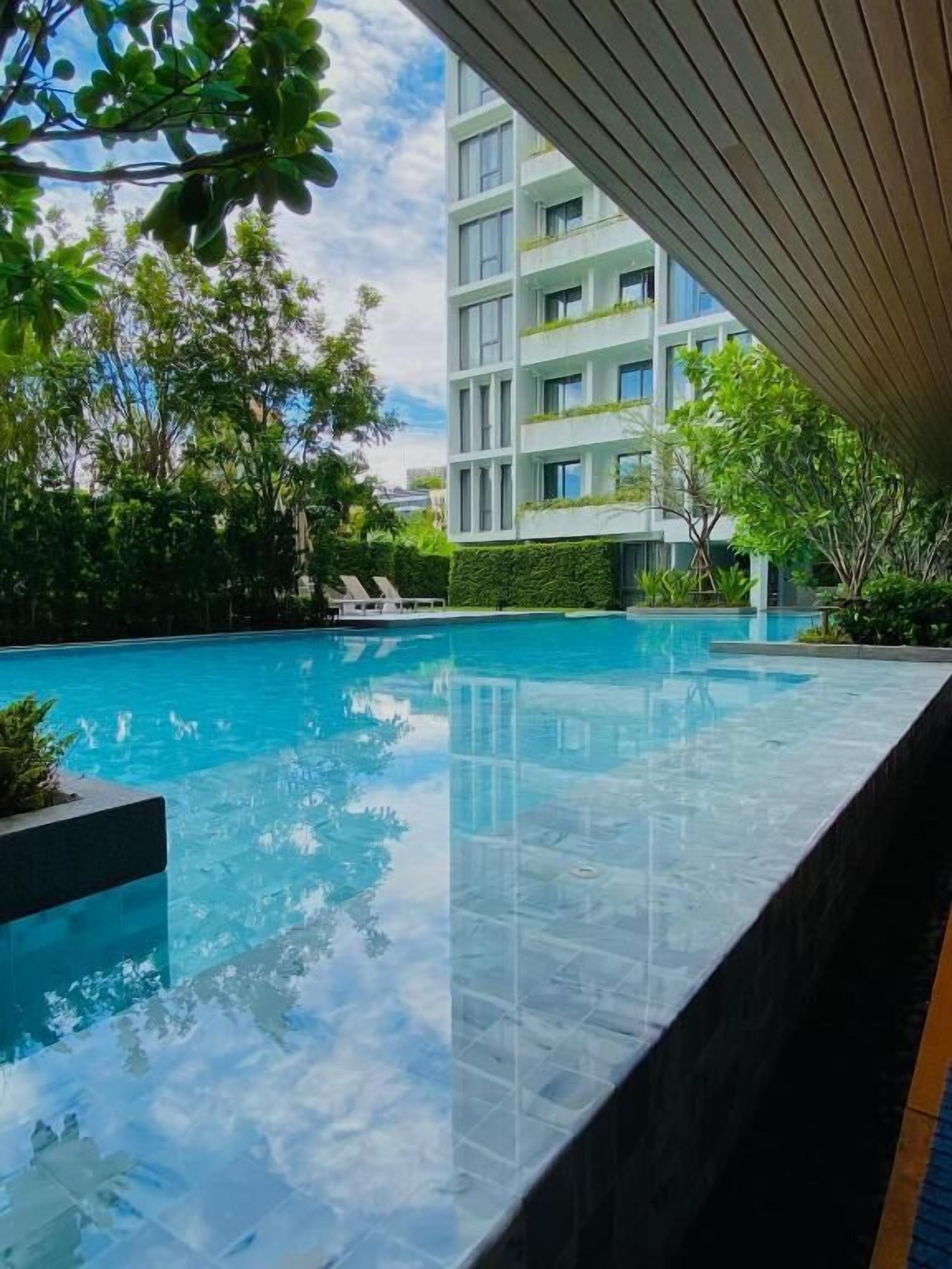 A modern building with a swimming pool, surrounded by greenery and clear skies.