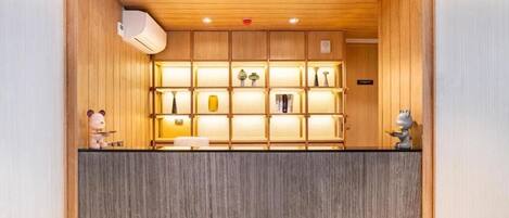 A reception area with a wooden ceiling, a grey reception desk, and shelves with various items.