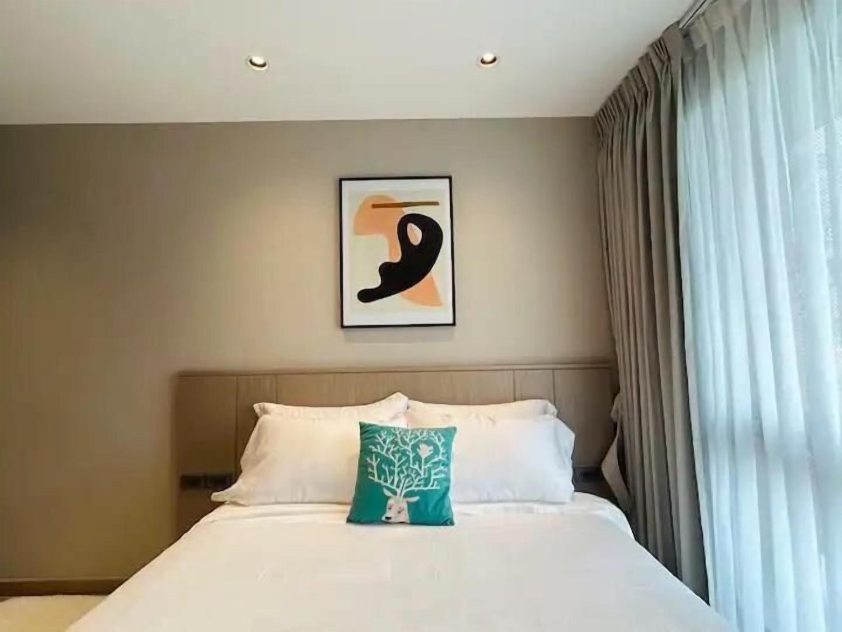 A hotel room with a bed, a headboard, a wall-mounted abstract painting, and a window with curtains.