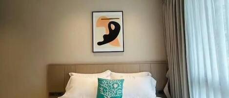 A hotel room with a bed, a headboard, a wall-mounted abstract painting, and a window with curtains.