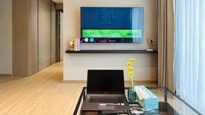 A modern living room with a flat-screen TV mounted on the wall, a laptop on a glass table, and a vase with yellow flowers. - Tierra Residence (Bangkok)
