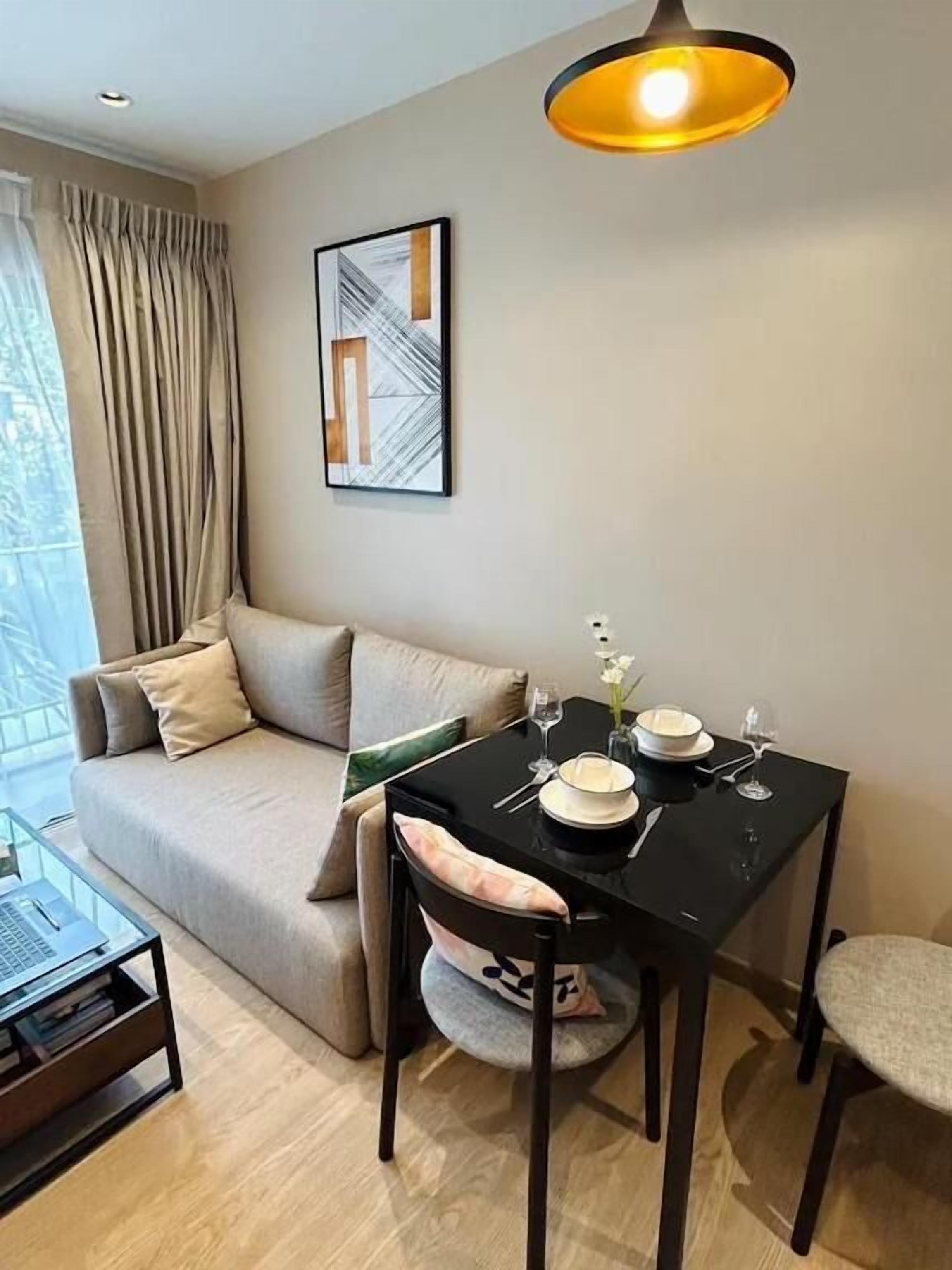 A modern living room with a sofa, a dining table set for two, and a pendant light.
