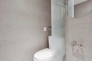 A modern bathroom with a toilet, a glass shower enclosure, and a wall-mounted faucet.