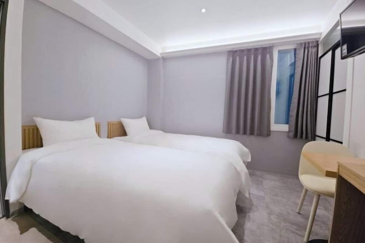 Une chambre d’hôtel avec deux lits, un bureau et une fenêtre avec des rideaux.