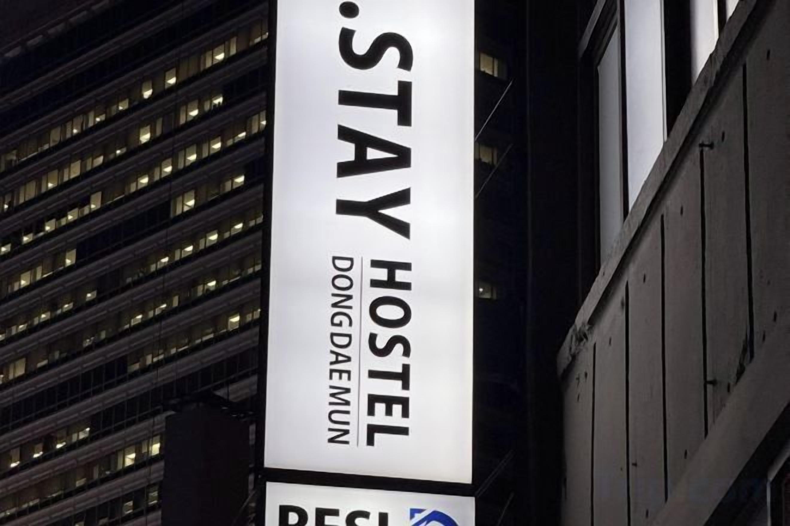 A vertical sign for Dongdaemun Hostel with a modern building in the background.