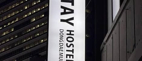 A vertical sign for Dongdaemun Hostel with a modern building in the background.