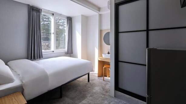 Una habitación de hotel moderna con cama, escritorio, silla, espejo y refrigerador.