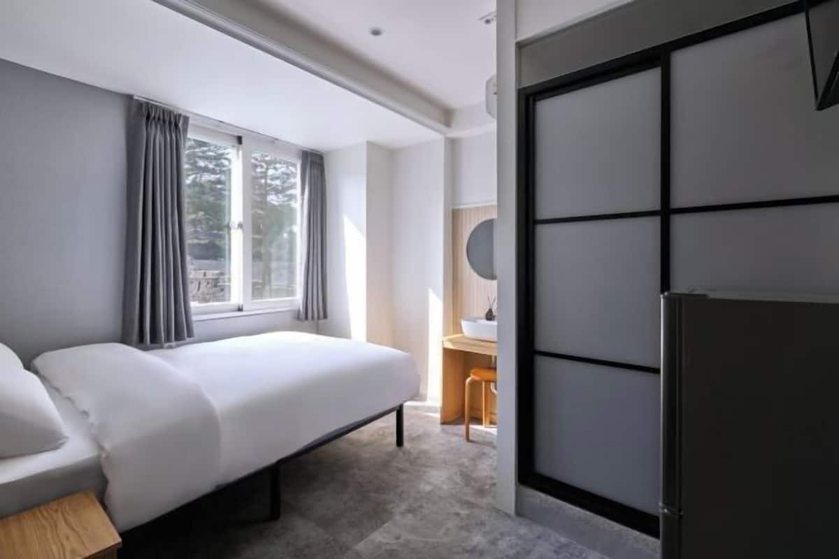 Une chambre d’hôtel moderne équipée d’un lit, d’un bureau, d’une chaise, d’un miroir et d’un réfrigérateur.