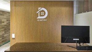 Un área de recepción con un revestimiento de listones de madera, un logo con el texto "D STAY" y un televisor de pantalla plana sobre un pedestal.