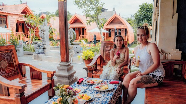 A wooden bench and table with a blue and white tablecloth, surrounded by potted plants and a statue. - Nusa Dua Huts Pondok Gajah Para by EPS (Nusa Dua)