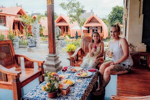 A wooden bench and table with a blue and white tablecloth, surrounded by potted plants and a statue. - Nusa Dua Huts Pondok Gajah Para by EPS (Nusa Dua)