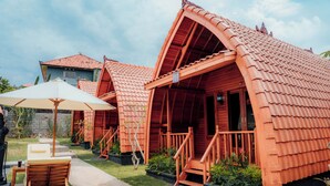 A row of wooden cabins with pitched roofs, a concrete pathway, and a wooden chair under an umbrella. - Nusa Dua Huts Pondok Gajah Para by EPS (Nusa Dua)