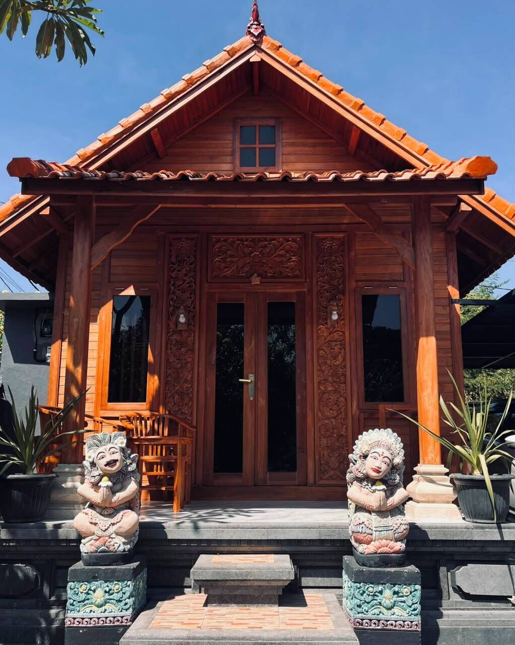 A traditional wooden building with a tiled roof, ornate carvings, and two stone statues at the entrance.