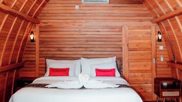 A wooden bedroom with a sloped ceiling, a bed with white and red bedding, and a small bedside table.